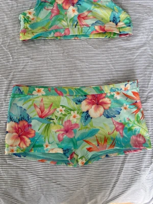 Blommig bikini med shortsmodell.Köpt i Spanien.ny pris sirka 800kr - Färgglad, stretchig bikini från banana moon med tropiskt blommönster i rosa, blått, grönt och orange. Överdelen är sportig med breda axelband och underdelen är i shortsmodell för extra komfort.midjan är 66cm och lårbredden är 40 cm.bredd på topp-66cm. resårbandet på toppen är något spröd.