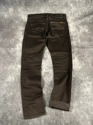 Svarta Nudie Jeans för herrar i vintageinspirerad 2000-talsstil i storlek W31 L32 - Enhetlig svart färg och en klassisk modell!  Skick: 9,5/10  Midja: 41 cm Benslut: 17 cm Lår: 28 cm Totallängd: 104 cm Måtten finns även på bilderna  Skickas inom ett dygn Spara på priset och frakten genom att sätta ihop ett paket! d152
