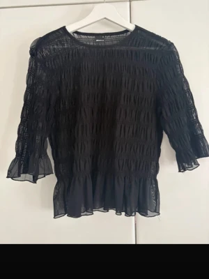ginatricot shirt - Säljer en svart transparent blus med trekvartsärm och volangdetaljer vid ärmslut och nederkant. Blusen har en luftig och lätt struktur med rynkade partier som ger en cool look. Perfekt att styla med jeans eller kjol.