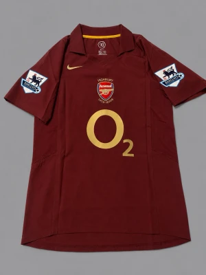 Arsenal matchtröja Highbury 2005/06 - Säljer en vinröd Arsenal matchtröja från säsongen 2005/06 med guldfärgade detaljer, klubbmärke och O2-logga framtill. På ryggen står det Henry 14 och Highbury 1913-2006. Korta ärmar och Premier League-patch på båda ärmarna. Perfekt för fotbollsfans! Helt nya! Pris kan sänkas vid snabb affär!