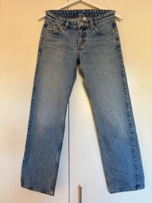 Blå raka jeans med låg midja, modell Arrow från Weekday, storlek 23/30 - Klassiska blå jeans med rak passform och låg midja. Jeansen har fem fickor, bälteshällor och knappgylf. Tillverkade i ett slitstarkt denimtyg som ger en tidlös look. Modell Arrow från Weekday, storlek 23/30. Mycket bra skick men svaga fläckar nedtill - se sista bilden.