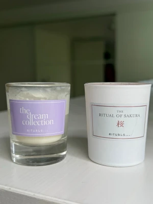 Doftljus Rituals Dream & Sakura - Två doftljus från Rituals: ett från The Dream Collection i glas med lila etikett och ett The Ritual of Sakura i vit behållare med rosa etikett. Ljusen har olika färg på vaxet, ett vitt och ett ljusrosa. Perfekt för att skapa mysig stämning hemma. Dom är använda! Båda för sammanlagt 10 kr😍