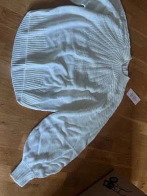Offwhite stickad tröja från Nelly - Säljer en offwhite stickad tröja från Nelly med rund halsringning och breda ribbade muddar vid ärmslut och nederkant. Tröjan har ett snyggt flätmönster upptill och ballongärmar som ger en trendig look.