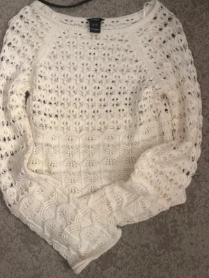 Vit virkad stickad tröja - Säljer en vit stickad tröja med virkat mönster och rund hals. Tröjan har långa ärmar och ett luftigt, genombrutet stickat material som ger en trendig look. Perfekt för lager på lager och passar till både jeans och kjol.