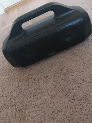 Soundcore svart bärbar högtalare - Säljer en svart bärbar högtalare från Soundcore med robust handtag och tydliga knappar för bass, bluetooth och power. Högtalaren har en stilren design i plast och metallgaller, perfekt för att ta med sig överallt och spela musik trådlöst.