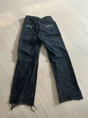 Svarta jeans  - Säljer ett par svarta jeans med raka ben och fransiga benslut. På bakfickorna finns vita broderade flammor. Storlek S och aldrig använda💕