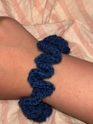 Blå virkad scrunchie - En scrunchie jag själv virkat i mörkblått garn och som har en volangig form. Perfekt för att piffa till en hästsvans eller använda som accessoar runt handleden. Ger en söt och trendig look till håret.  Jag virkar efter beställning, går att få i valfri färg och tjocklek🩷