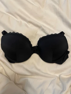 Svart bh med spetskant Victoria’s secret gamla modell  - Snygg svart bh med vadderade kupor och dekorativ spetskant upptill. Axelbanden är justerbara och bh:n har en liten rosett mellan kuporna.  Ingen lapp kvar. 