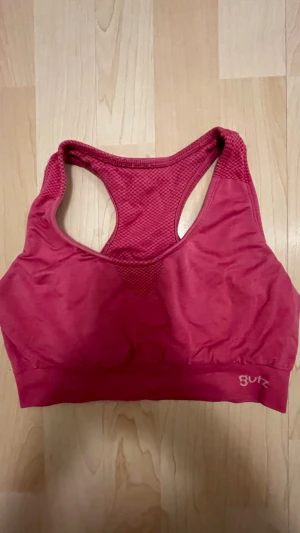 Röd sport-bh med meshdetaljer - Snygg röd sport-bh med brottarrygg och meshdetaljer för extra ventilation. Bh:n har bred resår nedtill och är tillverkad i ett stretchigt material som ger bra stöd. Perfekt för träning eller en aktiv vardag. Liten logga 'Butz' på nederkanten.