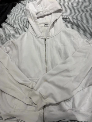 Vit zip hoodie från FB Sister - Säljer en vit hoodie från FB Sister i storlek XL. Hoodien har dragkedja framtill, två fickor och en klassisk huva. Tillverkad i mjukt och skönt material med borstad insida för extra komfort. Perfekt för en chill och avslappnad stil.
