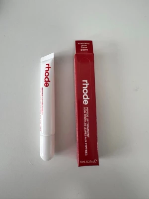 Rhode Peptide Lip Treatment Strawberry - Rhode Peptide Lip Treatment i smaken Strawberry Glaze. Läppbalsamet kommer i en vit tub med röd text och har en smidig applikator. Förpackningen är röd med vit text och rymmer 10 ml. Perfekt för att återfukta och ge glans till läpparna.