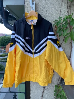 Vintage 90s Adidas Trefoil Vindjacka – Storlek XL - Vintage 90s Adidas Trefoil Vindjacka – Storlek XL Säljer en riktigt fet ikonisk original vintage vindjacka från Adidas, tillverkad tidigt 90-tal. Klassisk färgblock-design i gult, svart och vitt med ett snyggt geometriskt mönster över bröstet. Nyskick, oanvänd. Hör gärna av er vid frågor!