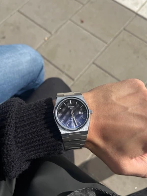 Tissot PRX blå svart Fade stållänk - Snygg Tissot PRX klocka med blå urtavla och datumvisning. Klockan har en stilren, fyrkantig boett och länk i rostfritt stål som ger en modern och clean look. Perfekt accessoar för dig som gillar klassisk men trendig stil.