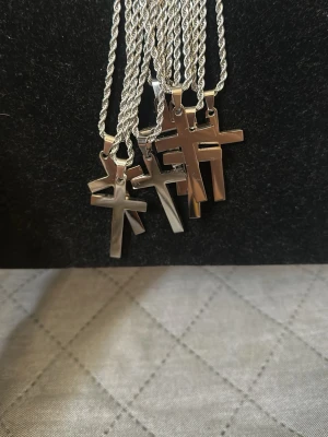 Silverfärgade korshalsband - Säljer flera stilrena halsband med korshängen i blankt silverfärgat stål. Kedjorna har tvinnad design och korsen är enkla och moderna. Perfekta för dig som gillar minimalistiska accessoarer med en klassisk touch. Finns 8st, 100kr st.