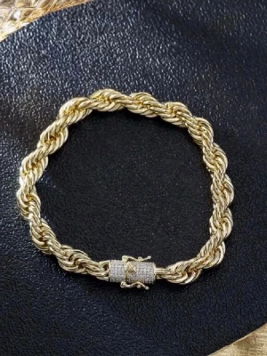 Guldfärgat tvinnat armband - Snyggt armband i guldfärgad metall med tvinnad design och ett lås dekorerat med små gnistrande stenar. Armbandet har en klassisk och stilren look som passar perfekt till din accessoar-samling.