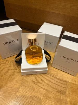Arquiste Aleksandr Eau de Parfum - Lyxig parfym från Arquiste i doften Aleksandr. Flaskan är rund med guldigt lock och genomskinligt glas som visar den bärnstensfärgade vätskan. Kommer i elegant vit förpackning med svart band och stilren design.