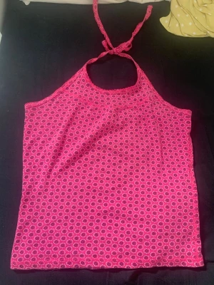 Rosa halterneck topp med blommönster - Säljer en rosa halterneck topp med små blommiga mönster. Toppen har knyt i nacken och är ärmlös, perfekt för varma dagar. Materialet känns mjukt och lätt, troligen bomull eller polyester. Snygg att styla till jeans eller kjol!