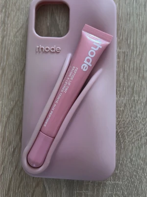 Rosa mobilskal rhode iPhone 12 - Snyggt ljusrosa mobilskal från rhode med unik ficka på baksidan, perfekt för att förvara småsaker som läppbalsam. Skalets mjuka material ger bra grepp och skydd till din mobil. Passar dig som vill ha både stil och funktion i ett.
