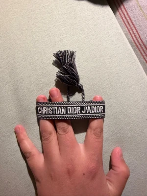  armband - Snyggt svart och vitt armband från Cmed texten ' broderad. Armbandet har justerbar knytning med tofsar och är gjort i textilmaterial. Perfekt accessoar för att lyfta din outfit.