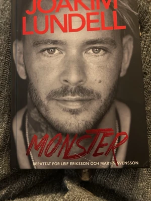 Monster av Joakim Lundell - En gripande bok med svart omslag och röd text, där Joakim Lundell berättar sin historia. Omslaget pryds av ett porträttfoto i gråskala och titeln 'Monster' i rött. Perfekt för dig som gillar självbiografiska romaner. Helt oläst men har stått framme så finns skavanker på omslaget