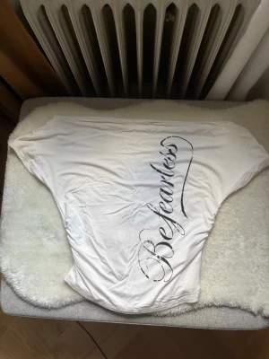 Vit t-shirt med texten Be fearless - Vit t-shirt med snyggt tryck i svart text som säger 'Be fearless' längs framsidan. Är perfekt för en cool och enkel stil. Använt 1 gång inna jag insåg att dne var för stor för mig