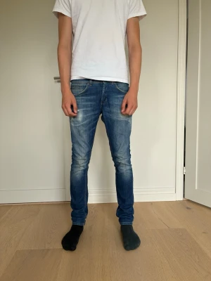 Dondup george - Säljer ett par blå slim fit jeans med snygga slitningar och tvättade detaljer. Modellen är dondup george