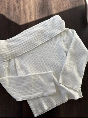 Vit ribbad off shoulder stickad tröja - Använd en gång. Trendig vit stickad tröja med ribbad struktur och bred off shoulder-krage. Långärmad modell i mjukt material som ger en snygg och avslappnad look. 