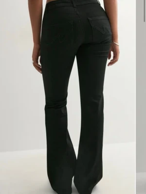 Svarta bootcut jeans med detaljer - Snygga svarta bootcut jeans med låg midja och dekorativa sömmar på bakfickorna från Nelly. Jeansen har en klassisk femficksmodell och är tillverkade i stretchigt denimtyg för en bekväm passform. Perfekta för dig som gillar en tidlös men trendig look.