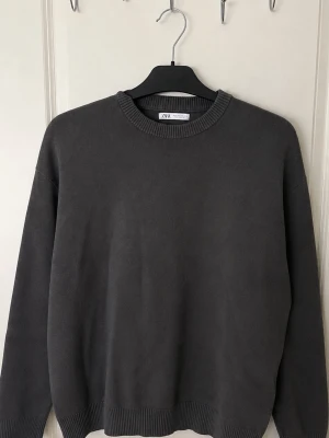 Mörkgrå sweatshirt från Zara - En stilren mörkgrå sweatshirt från Zara med rund halsringning och ribbade muddar vid ärmslut och nederkant. Perfekt för en avslappnad och enkel look. Passar till det mesta och är lätt att matcha.