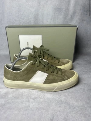 Tom Ford skor - Snygga olivgröna sneakers med vit sula och en vit rand på sidan. Skorna har klassisk låg profil, snörning och ovandel i mockaliknande material. Perfekta för en avslappnad streetstil.