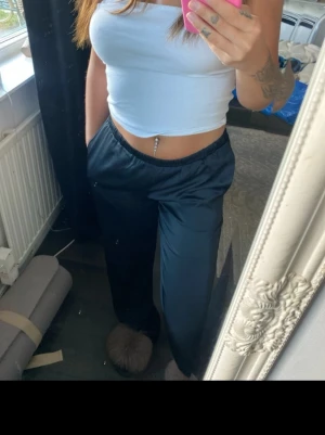 Svarta vida loungewear-byxor - Säljer ett par svarta, vida loungewear-byxor med resår i midjan. Byxorna har en avslappnad passform och är perfekta för hemmamys men också till vardags. Materialet är mjukt och glansigt, vilket ger en skön känsla mot huden. 