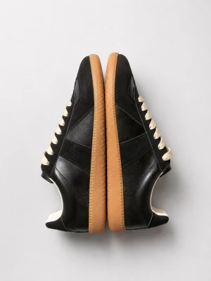Maison Margielas - Stilrena svarta sneakers med beige gummisula och vita snören. Skorna har en klassisk låg profil och är tillverkade i slätt läder med diskreta paneldetaljer. Perfekta för en clean och tidlös look.