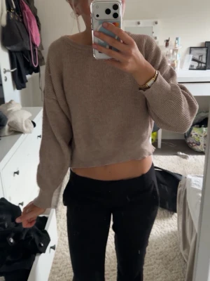Beige croppad stickad tröja med knyt - Säljer en beige croppad stickad tröja med lång ärm och snygg knyt-detalj i ryggen. Tröjan har en avslappnad passform och är perfekt för dig som gillar en enkel men trendig stil.