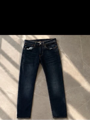 Mörkblå slim jeans - Säljer ett par mörkblå jeans med rak passform och klassisk femficksdesign. Jeansen har kontrastsömmar och knappgylf. Materialet är denim i bomull och de har en tidlös look som passar till det mesta.