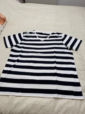 Randig t-shirt från Bläck - Säljer en klassisk randig t-shirt från Bläck i storlek XXL. T-shirten har breda marinblå och vita ränder, v-ringad hals och korta ärmar. Tillverkad i mjuk bomull som känns skön mot huden. Perfekt för en avslappnad och stilren look.
