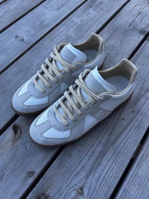 Maison Margiela Gats - Hej! Jag säljer ett par Maison Margiela GATs i fint skick, storlek 43. Den typiska vita färgen, skitsnygga.  Inköpsbevis visas vid intresse. Köptes ett tag sedan och har knappt använts.  Skor, box och dustbag medföljer. Säljer av lite plagg från garderoben nu. Skriv om ni har några som helst frågor. Säljer för 2550kr.