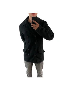 Svart dubbelknäppt rock - Stilren svart rock med dubbelknäppning och bred krage. Rocken har två fickor med lock framtill och en rak passform. Perfekt för dig som vill ha en klassisk look med modern touch. Rocken är i storlek L men passar även M Personen i bilden är 180cm 69kg och bär vanligtvis storlek M