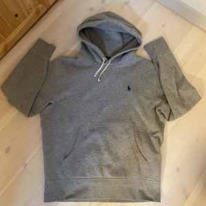 HOODIE | RALPH LAUREN. - Säljer en klassisk grå hoodie med huva och dragsnören. Tröjan har en stor magficka och en liten broderad logga på bröstet. Perfekt för chill dagar och enkel att matcha med jeans eller mjukisbyxor.