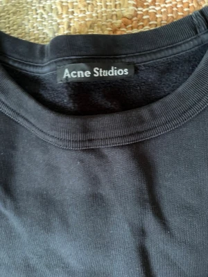 Svart sweatshirt från Acne Studios - Klassisk svart sweatshirt från Acne Studios med rund halsringning och ribbade muddar vid ärmslut och nederkant. Tröjan har en enkel och stilren design, perfekt för en avslappnad look. Tillverkad i mjukt bomullsmaterial.