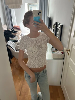 Vit spetsig croppad topp - Säljer en vit croppad topp i spets med korta ärmar. Toppen har ett genombrutet blommigt mönster och sitter tight mot kroppen. Perfekt för dig som vill ha en trendig och feminin look.