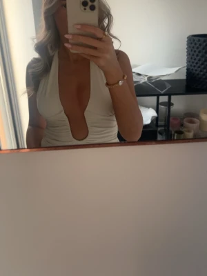 Vit body med djup urringning - Säljer en beige body med omlottdesign och djup v-ringning. Bodyn är ärmlös och har en stilren, figurnära passform som framhäver siluetten. Perfekt för sommarens alla tillfällen.