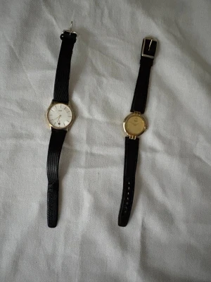 Citizen Quartz klocka med svart band - 2 st Citizen quartz klockor i fint skick. Den ena i guldfärg och 28 mm på uret. Den andra med datumfunktion och 31 mm på uret. De tickar inte just nu, vet ej varför. I övrigt fina skick på klockorna och bandet.   Japanska urverk i klockorna. Få repor på glasen.  Den vita klockan är grön på 2 ställen på glaset, se bilder. Det verkar vara lite damm på uret också.  180 kr / st 300 kr för båda.  Priset kan diskuteras.  Säljes i befintligt skick. 