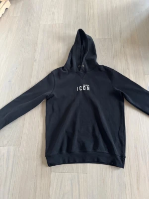 Svart hoodie från Dsquared2 ICON - Snygg svart hoodie från Dsquared2 med 'ICON' tryck på bröstet. Klassisk modell med huva och dragsko, tillverkad i mjukt bomullsmaterial. Perfekt för dig som vill ha en stilren och trendig look.OBS!! Den är liten för storleken så den är typ en medium 