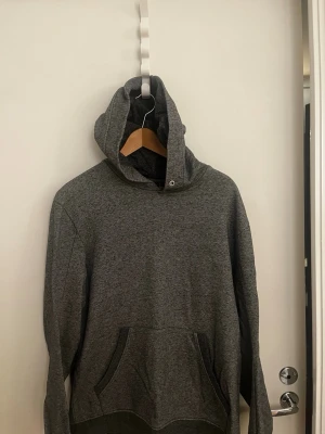 Grå hoodie från J.Lindeberg - Snygg grå hoodie från J.Lindeberg med klassisk känguruficka och huva. Tillverkad i mjukt material som känns skönt mot huden. Perfekt för en avslappnad och stilren look.