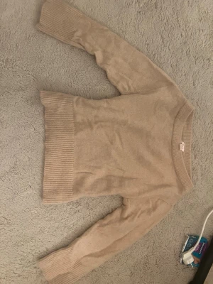 Beige stickad tröja med bred mudd - Mysig beige stickad tröja med rund halsringning och bred ribbad mudd vid ärmslut och nederkant. Tröjan har en enkel och stilren design som passar perfekt till många olika outfits. Materialet ser mjukt och bekvämt ut, perfekt för kyligare dagar. Passar ej mig och därav används inte.