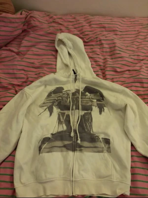 Vit hoodie Billie Eilish  - Säljer en vit hoodie med huva och dragkedja framtill. På framsidan finns ett stort svartvitt tryck med motiv av Billie Eilish. Hoodien har snören i huvan och är i en avslappnad passform.🤍🩶🖤