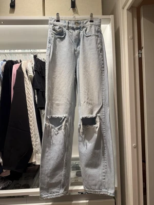  Straight jeans med stora hål - Säljer ett par ljusblå raka jeans med stora slitna hål över knäna. De är lite utsvängda längst ner men inte super mycket. Jeansen har klassisk femficksmodell och hög midja. Materialet är denim i bomull och passformen är relaxed och trendig. Midjemått 31 cm , 28 från skrevet till midjan, och 71cm i inrebenslängd. Snygga att sy om till lågmidjatt eller  behålla som de är.
