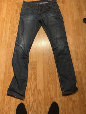 Mörkblå raka jeans herr - Säljer ett par mörkblå jeans med lite bootcut och klassisk femficksmodell. Jeansen har slitningar och skrynkliga detaljer för en avslappnad look. Materialet är denim i bomull och passformen är normal. Perfekta till en casual stil. Pris kan diskuteras 