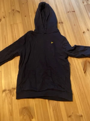 lyle and scott hoodie  - Snygg mörkblå hoodie med huva och magficka. På bröstet finns en lyle and scott fågel. Hoodien har en klassisk passform och är tillverkad i mjukt material, perfekt för en avslappnad stil.