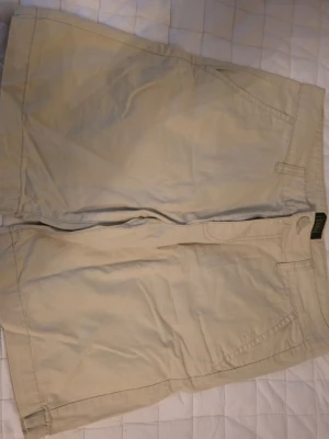 Beige shorts från Solid, storlek M - Säljer ett par klassiska beige shorts från Solid i storlek M. De har en enkel design med fickor fram och dragkedja. Perfekta för varma dagar och lätta att matcha med olika stilar.